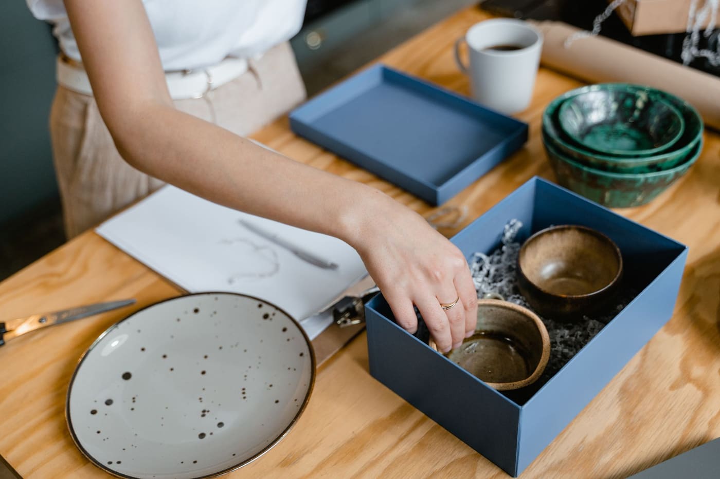 A person packing handmade ceramic bowls into a box at a wooden table