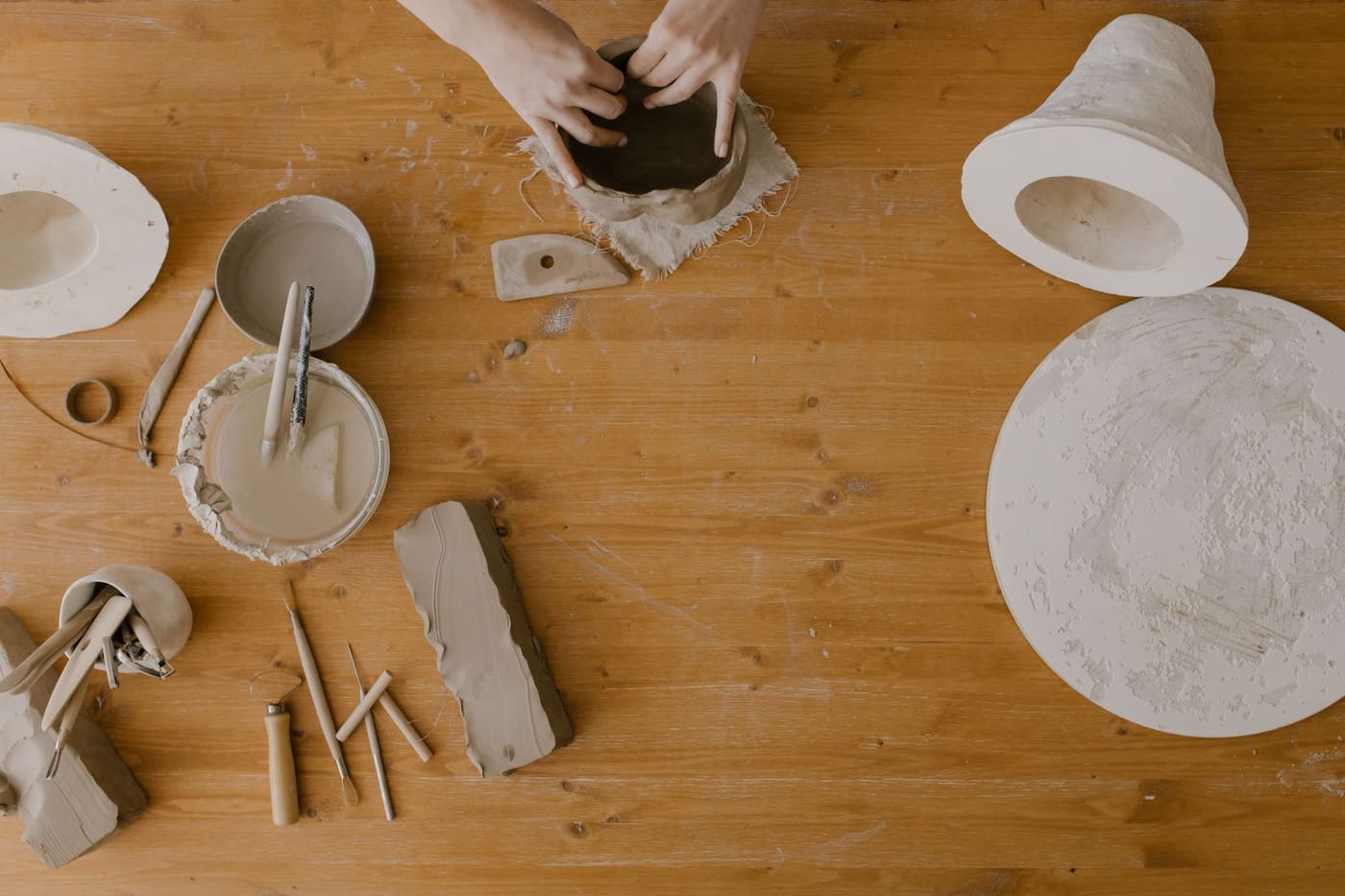 Overhead view of hands shaping clay with tools on a wooden workshop table