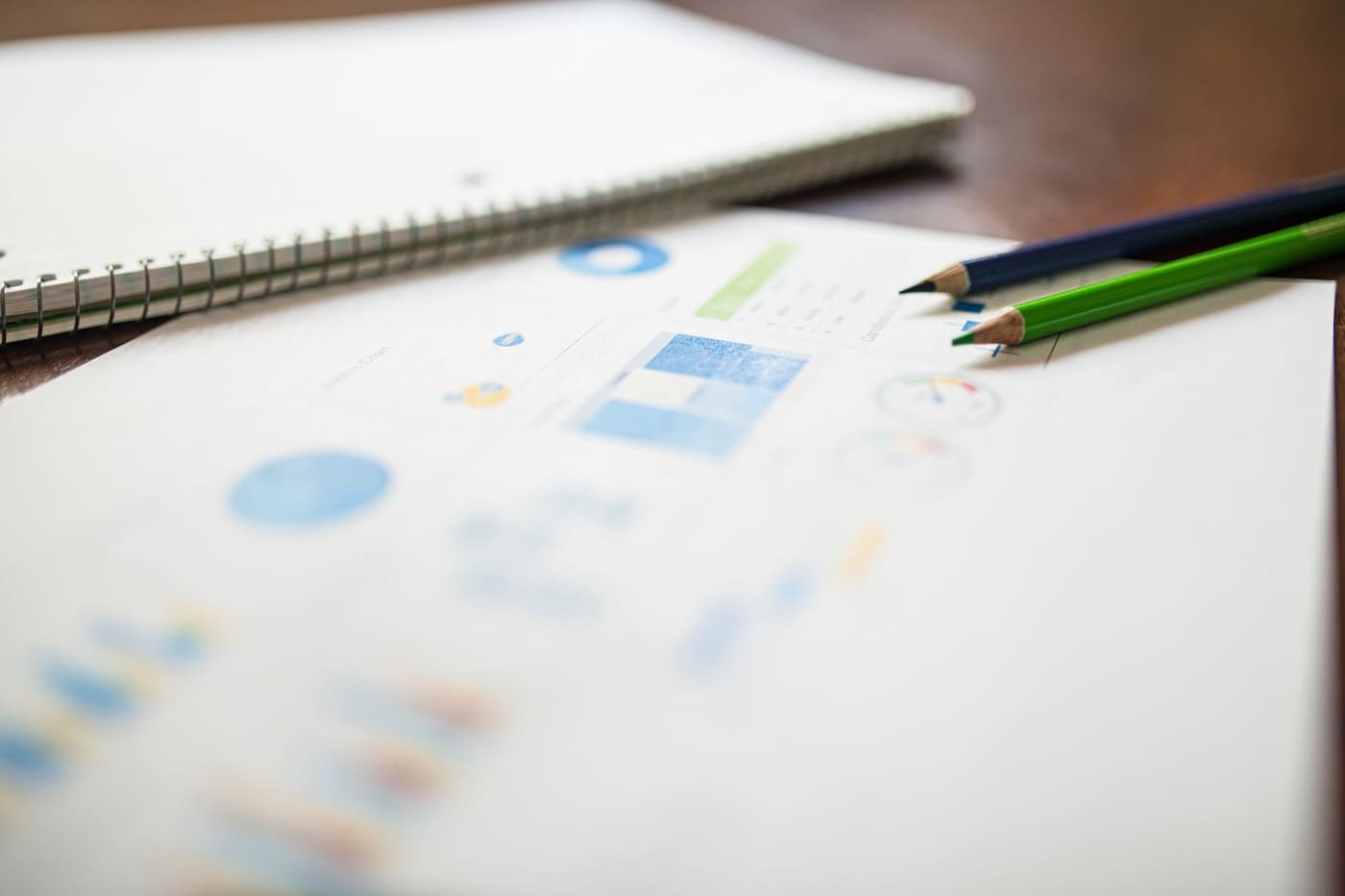 Two colored pencils and a spiral notebook resting on a printed report with charts