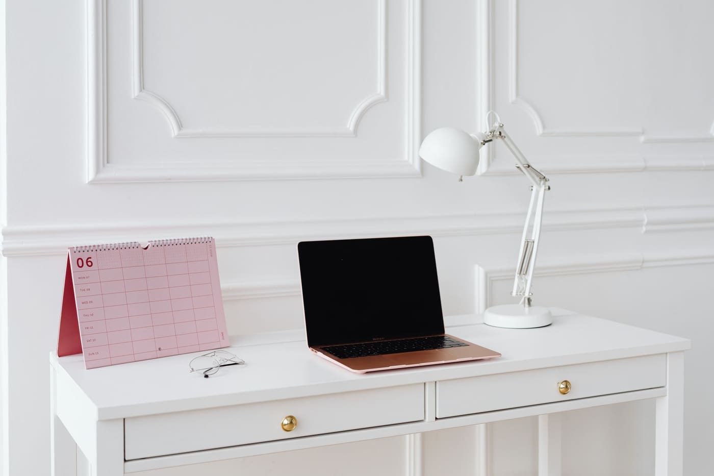 A tidy white desk with a laptop and wall calendar in a bright room