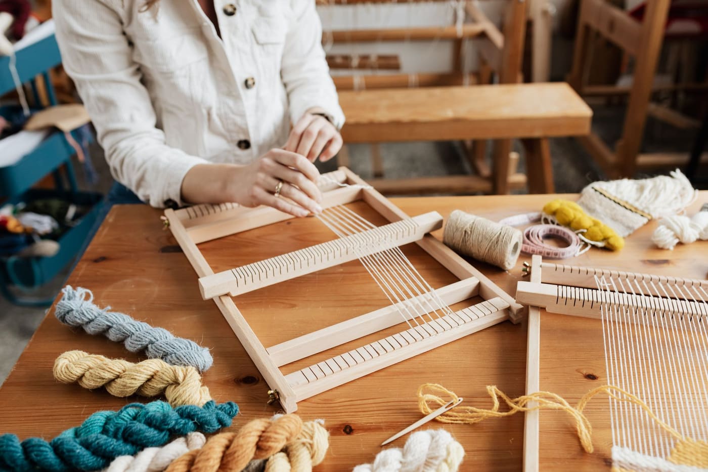 Hands weaving yarn on a small wooden loom