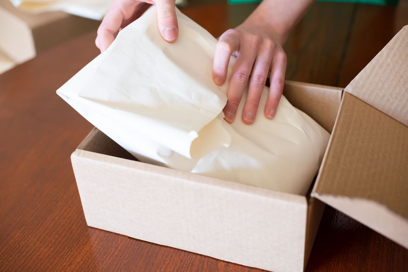 Hands wrapping an item in paper inside a cardboard box