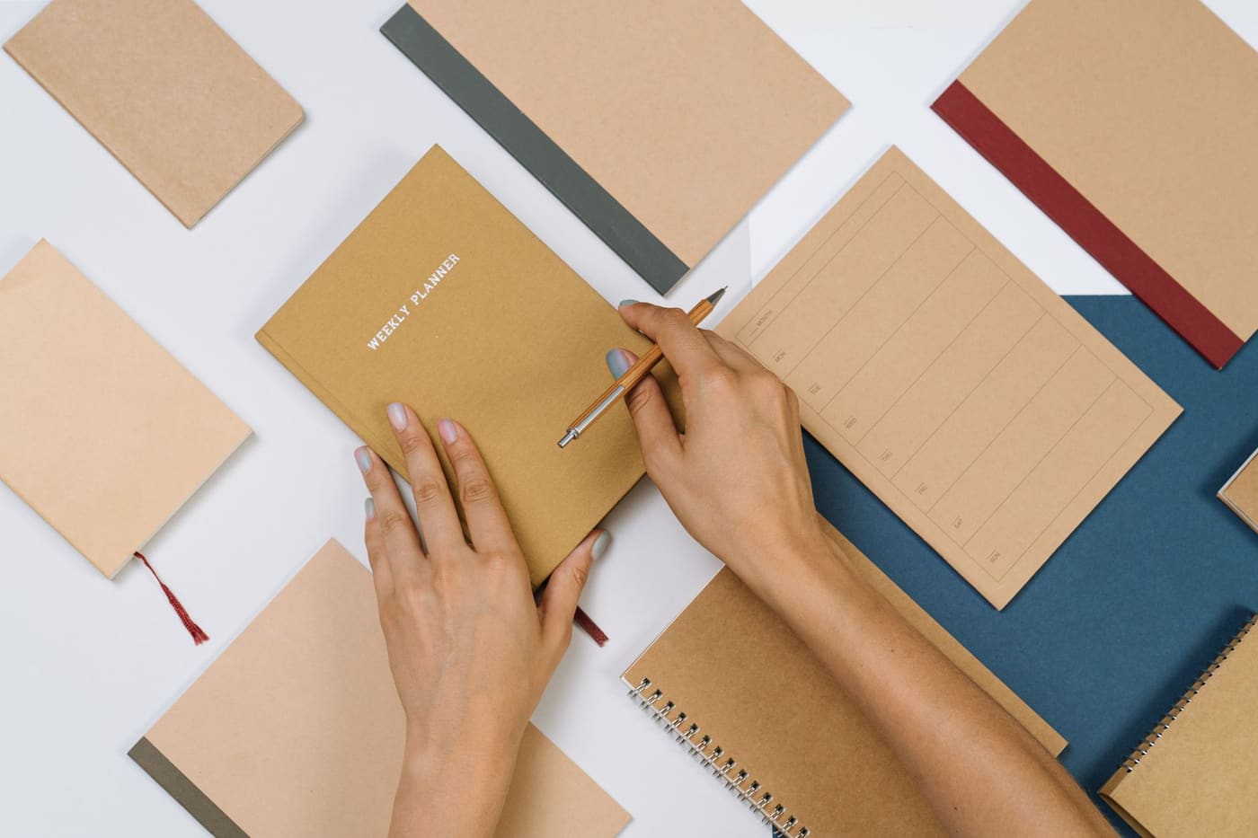 Hands writing in a planner on a desk surrounded by notebooks