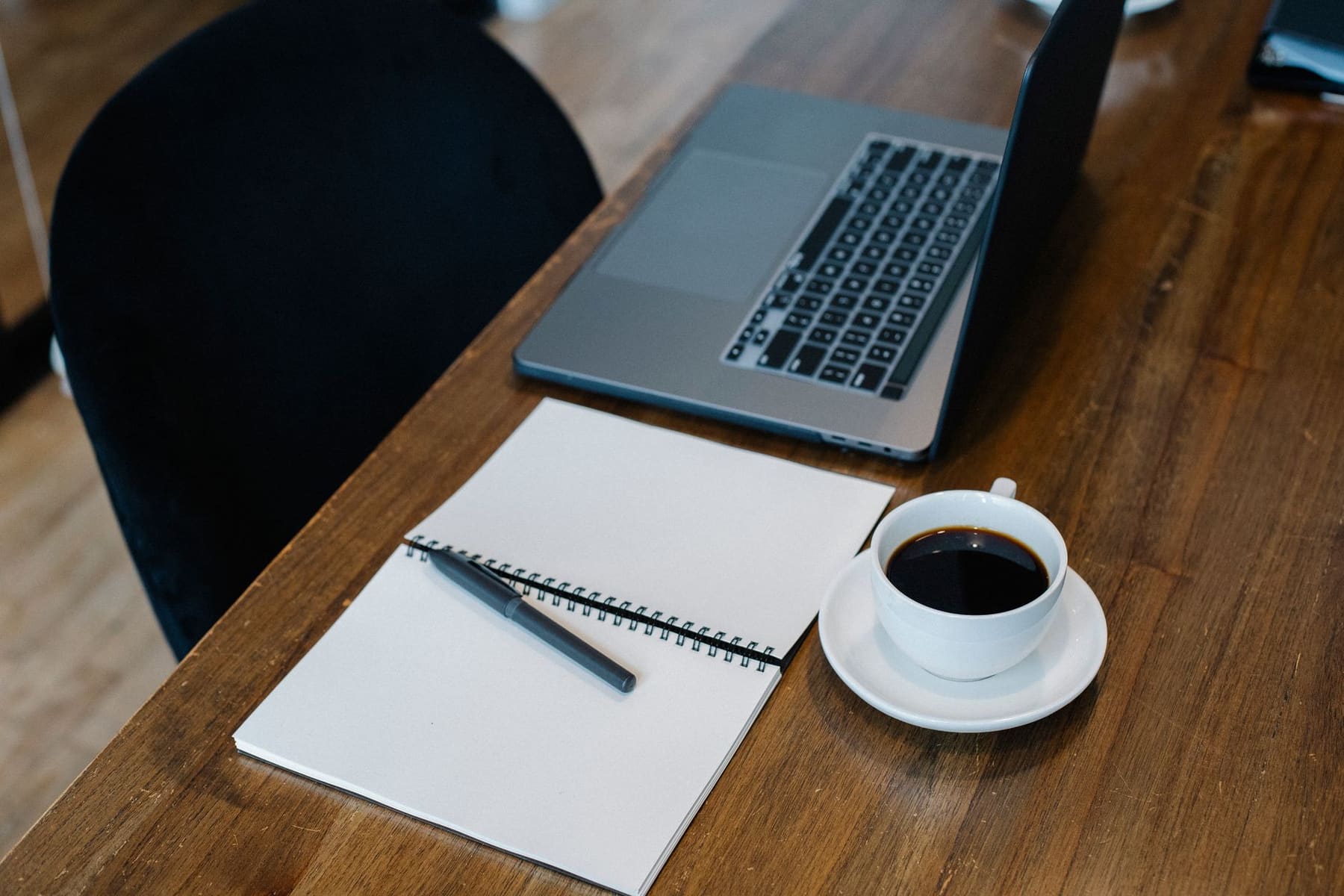 Open laptop, notebook and a cup of coffee on a wooden desk