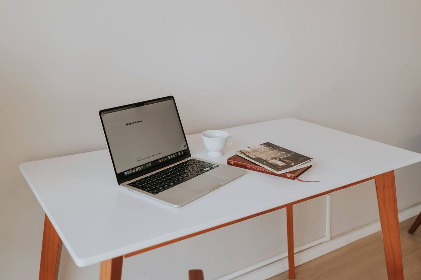 A white desk with a laptop, coffee cup and a few books