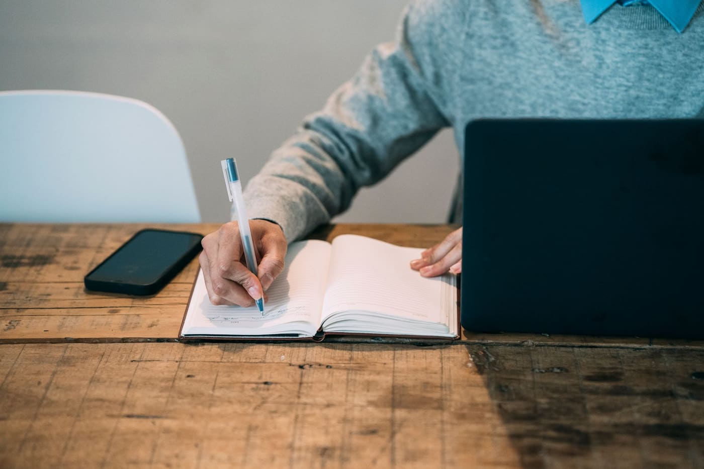 A notebook and pen on a wooden table beside a laptop