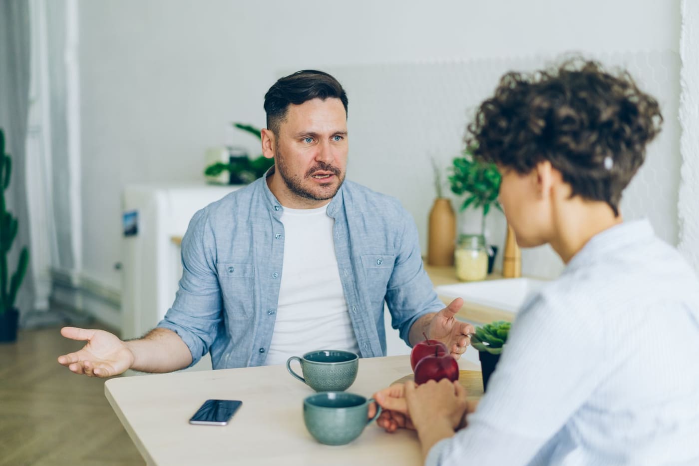 Two adults talking at a kitchen table with coffee cups