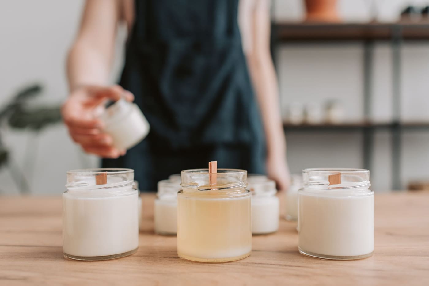 A woman pouring soy candles on a wooden table in a small workshop