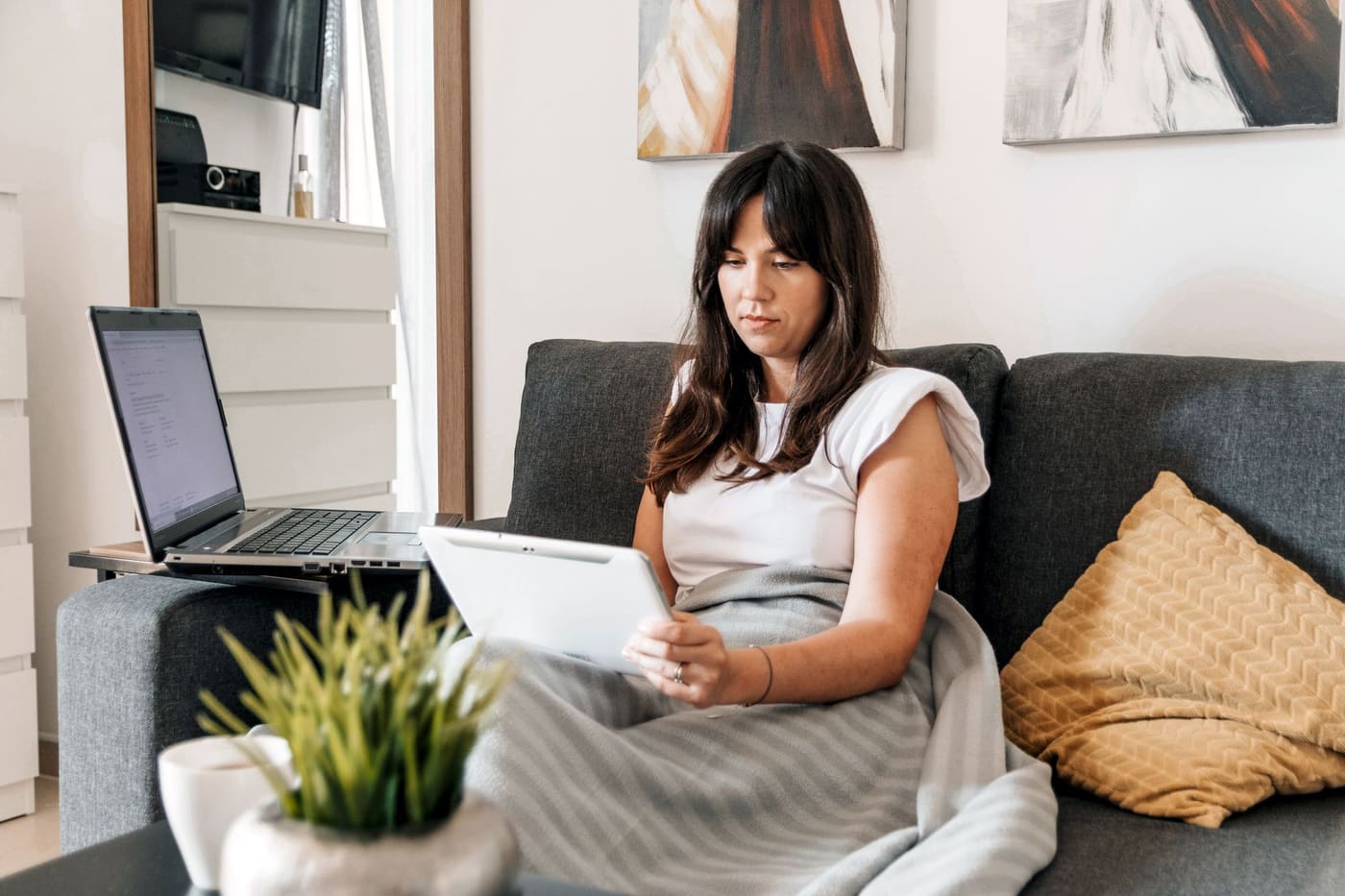 A woman on a sofa with a tablet and a blanket